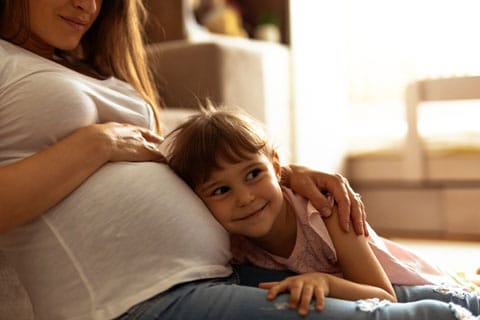 Little girl resting ear on pregnant mom’s belly